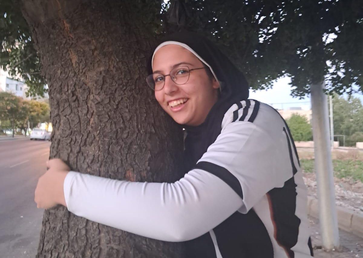 Girl wearing a black hijab hugging a tree