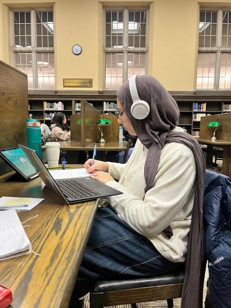 Girl wearing a hijab and headphones studying in a library
